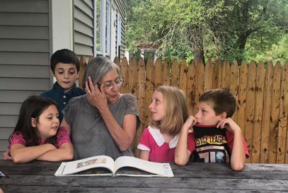 group of children with adult at table with book