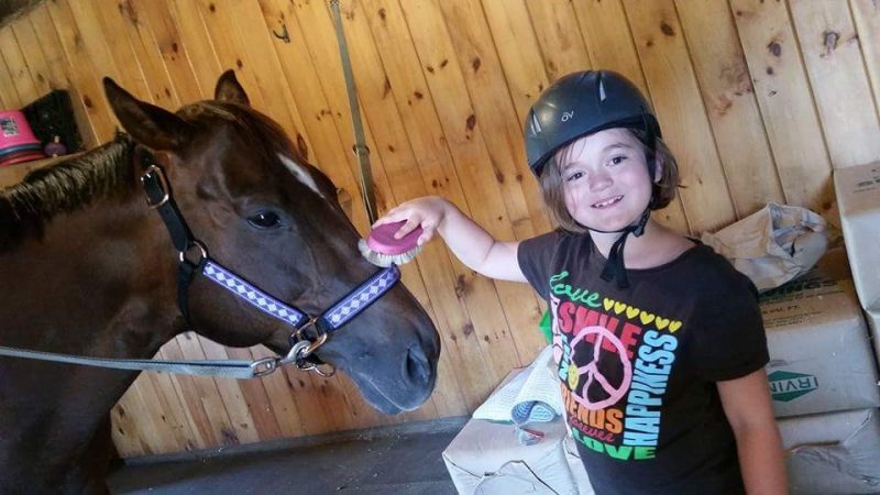 girl with helmet petting a horse